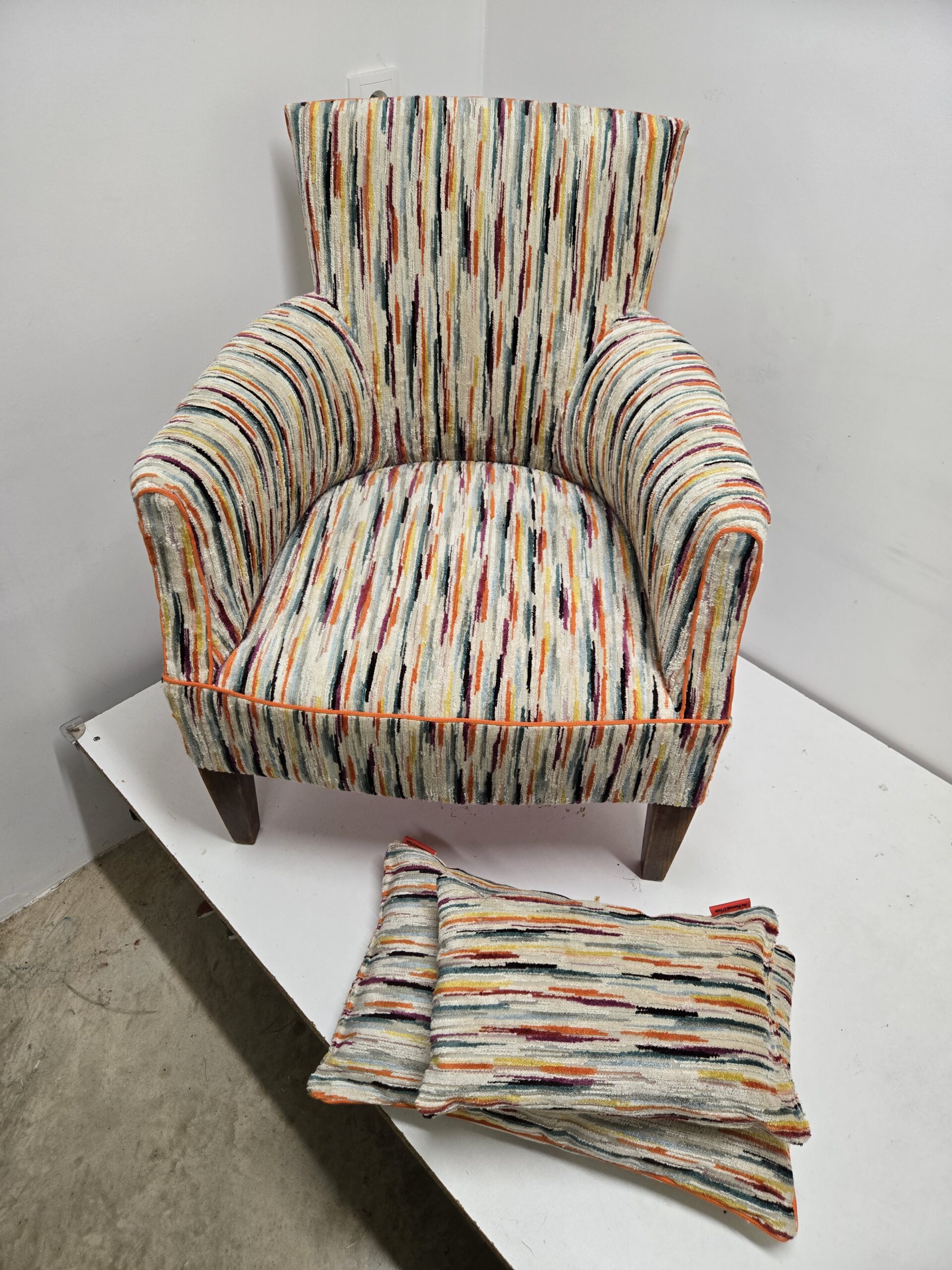 fauteuil des années 30 avec un tissu multicolore en fausse rayures posé sur un plan de travail de l'atelier et ces 2 coussins assortis.