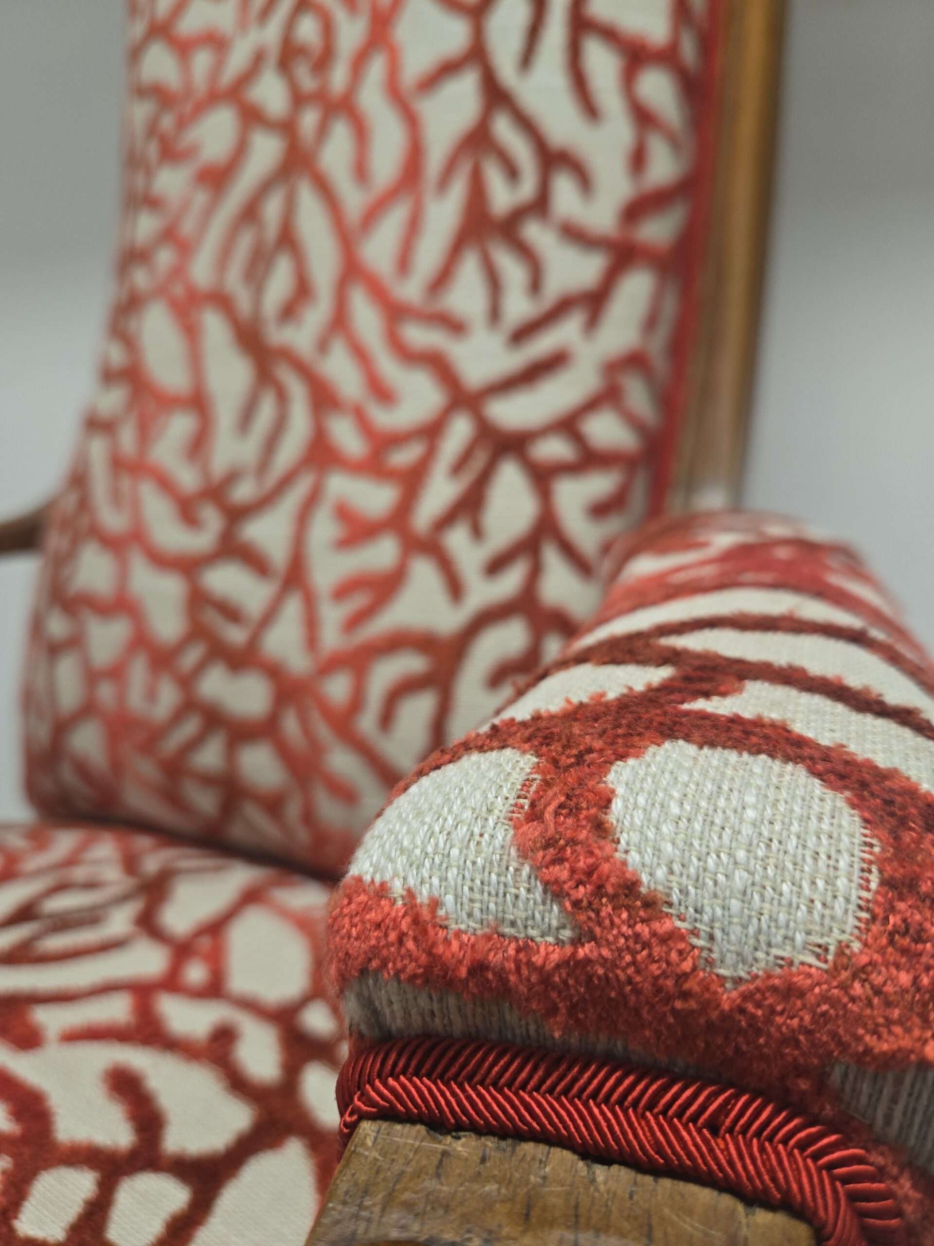 détail d'un accoudoir du voltaire au tissu corail rouge sur fond beige ou l'on voit le relief du velours
