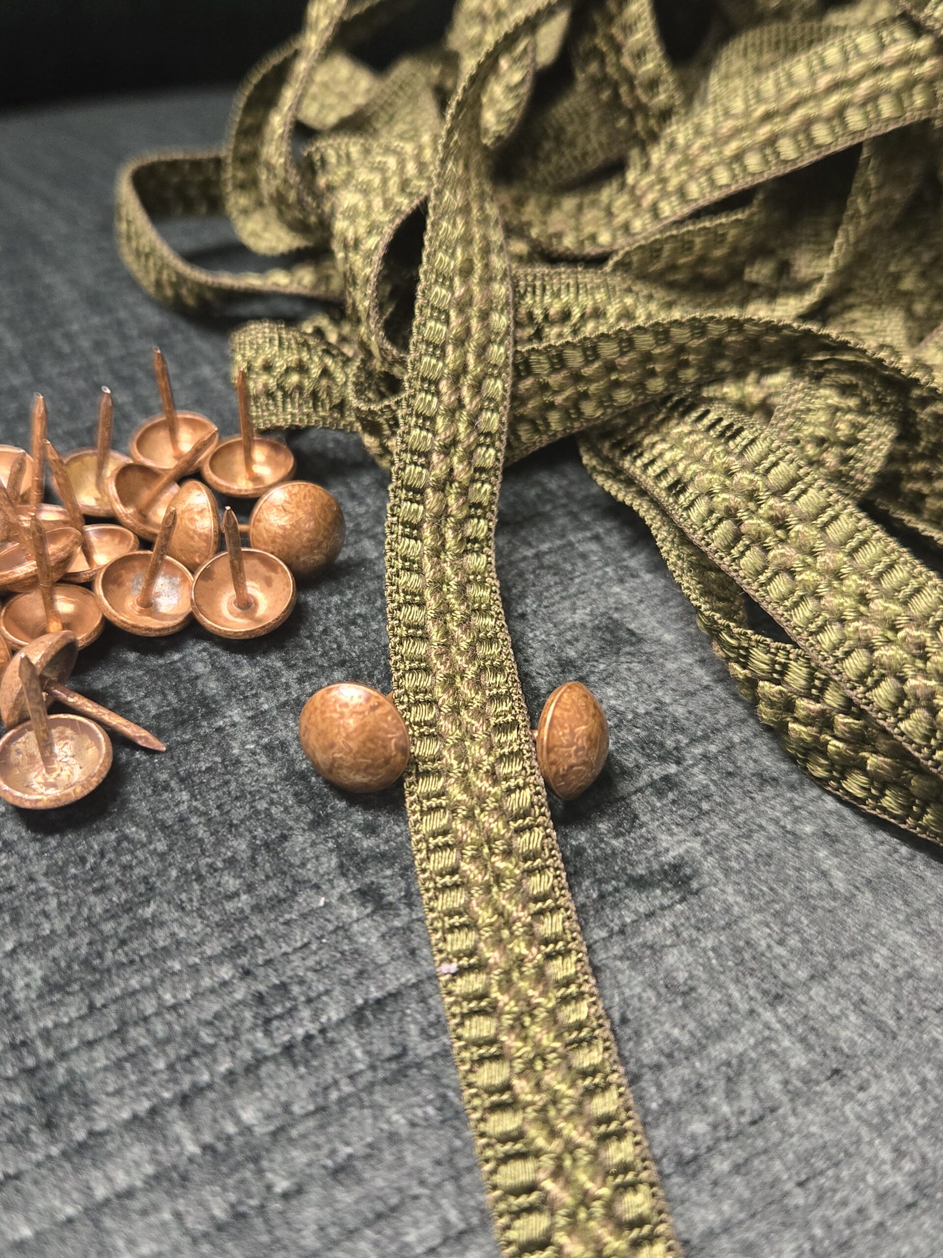 détail de clou et galon plat posé sur un velours vert bouteille