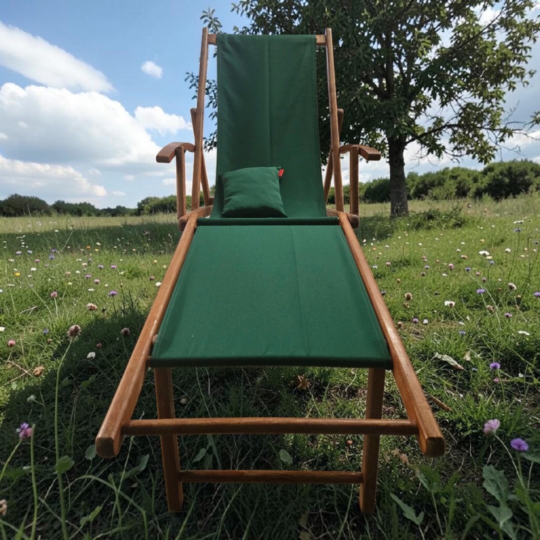 1chilienne ancienne en teck avec repose pied, et un tissu outdoor vert bouteille dans un décor de prairie fleuri vue de face avec son coussin repose tête assorti